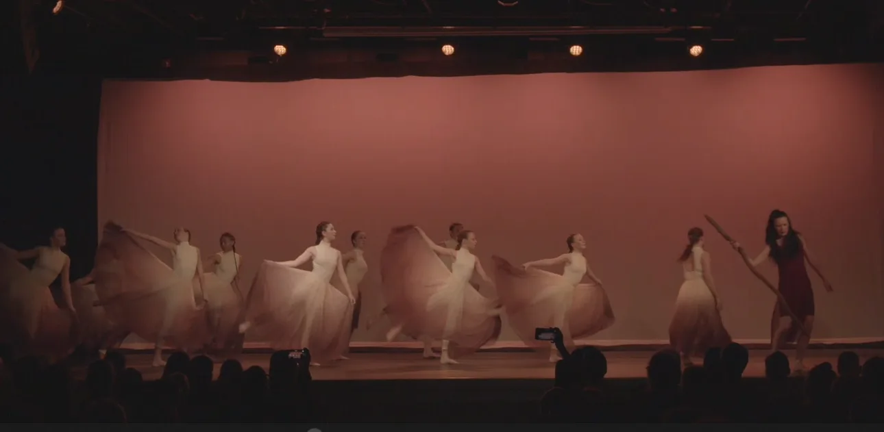 Dancers in flowing pale costumes before a warm pink backdrop.