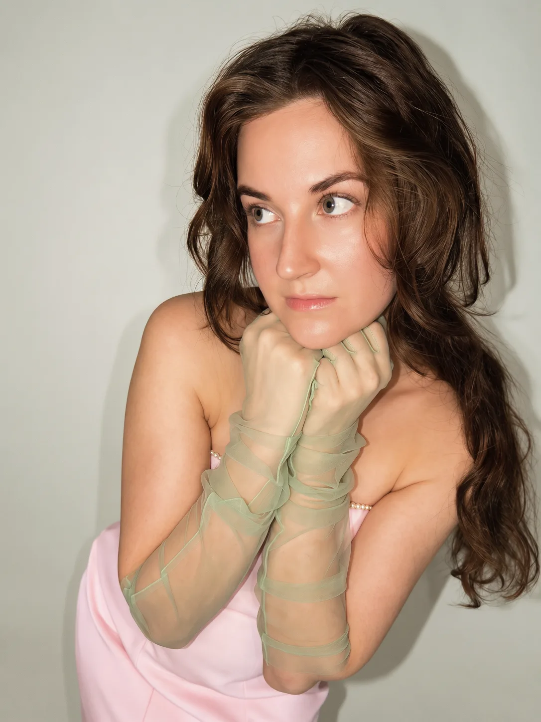 A close-up portrait of a woman in a pink dress wearing pale green gloves.