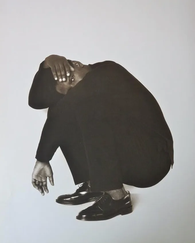 A dancer in black crouched low with head bowed, arms wrapped over the head.
